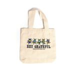 Canvas bag featuring five vibrant, cartoon-style bees in various colors, inspired by the 'Grateful Dead' bears, with black text that reads 'Bee Grateful'.